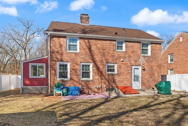 rear view of house featuring brick siding, a lawn, a chimney, and fence