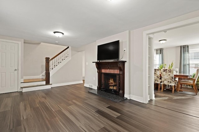 unfurnished living room with baseboards, a lit fireplace, wood finished floors, and stairs