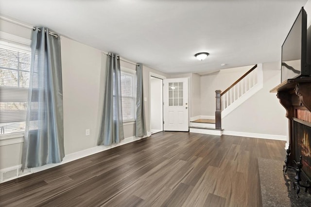 foyer entrance with stairway, baseboards, a lit fireplace, and wood finished floors