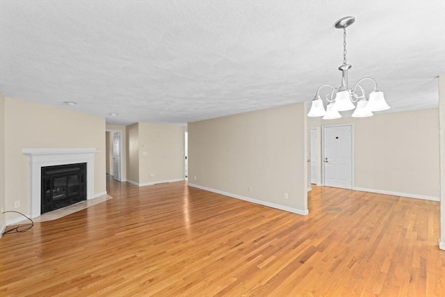 225 Lincoln St Unit G3, Duxbury, MA 02332 - unfurnished living room featuring a textured ceiling, light wood finished floors, a chandelier, and a fireplace with flush hearth
