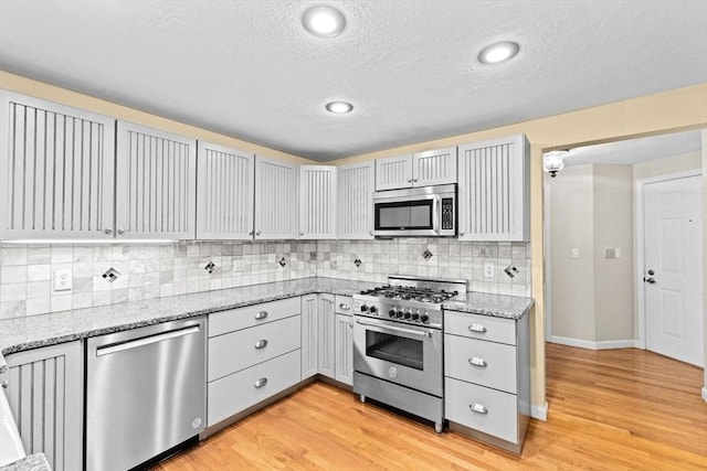 225 Lincoln St Unit G3, Duxbury, MA 02332 - kitchen with appliances with stainless steel finishes, a textured ceiling, light wood-style flooring, light stone counters, and backsplash