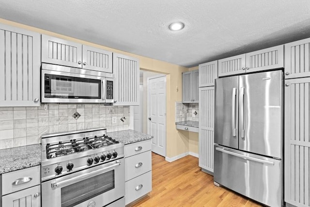 225 Lincoln St Unit G3, Duxbury, MA 02332 - kitchen featuring appliances with stainless steel finishes, a textured ceiling, light wood-style floors, decorative backsplash, and light stone countertops