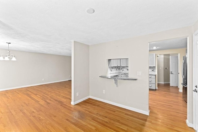 225 Lincoln St Unit G3, Duxbury, MA 02332 - unfurnished living room with light wood-style floors, a textured ceiling, and a chandelier