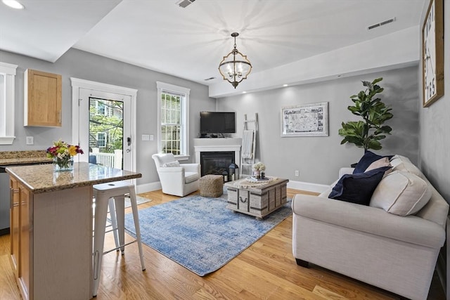 living area with a glass covered fireplace, light wood-style flooring, and baseboards