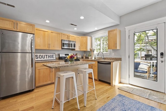 kitchen featuring visible vents, a kitchen breakfast bar, a center island, light stone countertops, and stainless steel appliances