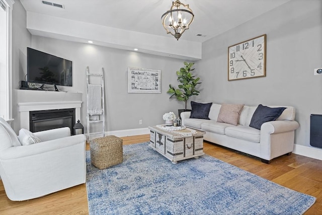 living area featuring a glass covered fireplace, wood finished floors, visible vents, and baseboards