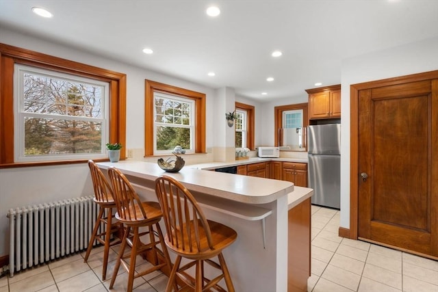 kitchen with a peninsula, a breakfast bar area, freestanding refrigerator, and radiator