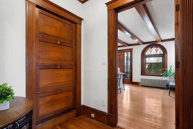 foyer entrance featuring vaulted ceiling with beams, light wood finished floors, radiator heating unit, and baseboards