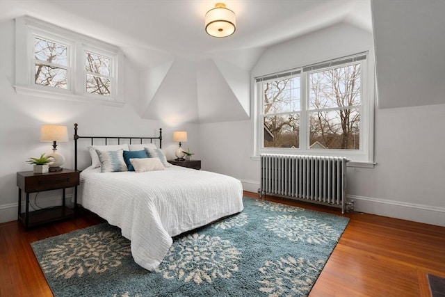 bedroom featuring lofted ceiling, radiator, multiple windows, and wood finished floors