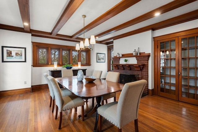 dining space with baseboards, hardwood / wood-style floors, beamed ceiling, a brick fireplace, and a notable chandelier