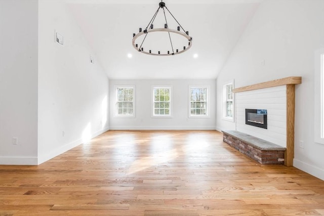 unfurnished living room featuring light wood-type flooring, a brick fireplace, and high vaulted ceiling