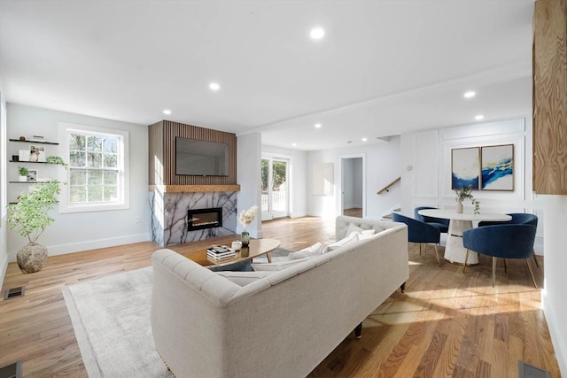 living room with light wood finished floors, recessed lighting, visible vents, a premium fireplace, and baseboards