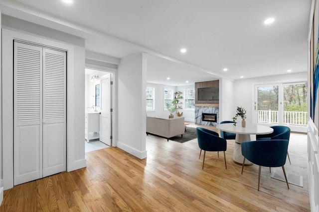 dining room featuring a healthy amount of sunlight, a premium fireplace, and light hardwood / wood-style floors