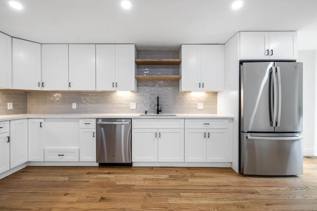 kitchen featuring white cabinets, appliances with stainless steel finishes, light hardwood / wood-style floors, sink, and backsplash