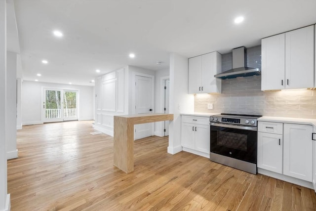 kitchen with light wood-type flooring, wall chimney range hood, stainless steel electric stove, and white cabinetry