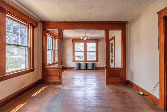 empty room featuring a textured ceiling, radiator, dark wood-type flooring, ornate columns, and a chandelier