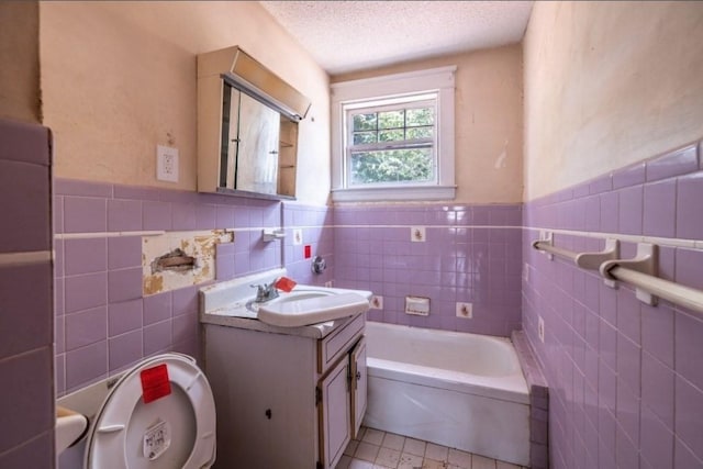 bathroom with vanity, a washtub, tile walls, and a textured ceiling