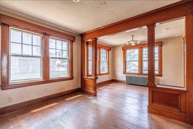 unfurnished room featuring radiator heating unit, ornate columns, hardwood / wood-style floors, a textured ceiling, and a notable chandelier