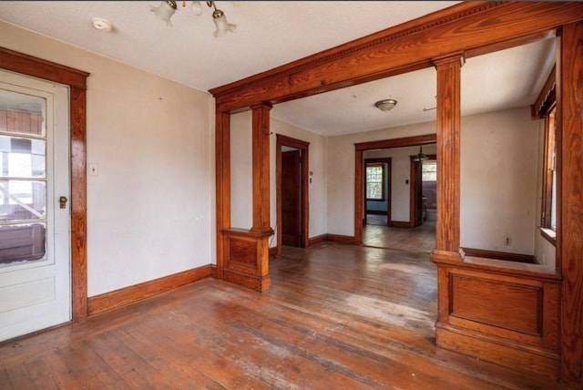 empty room featuring decorative columns and dark hardwood / wood-style flooring