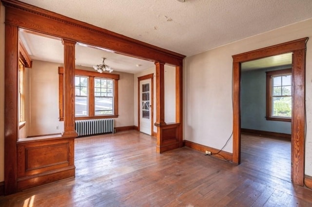 unfurnished room featuring radiator heating unit, hardwood / wood-style floors, a textured ceiling, and ornate columns