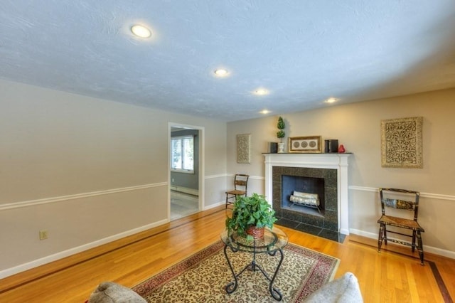 living room with a tile fireplace, wood-type flooring, a textured ceiling, and a baseboard radiator