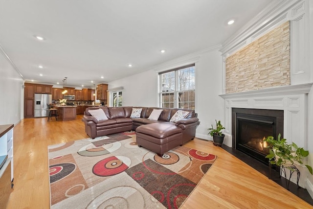 living area featuring a fireplace with flush hearth, recessed lighting, light wood-type flooring, and ornamental molding