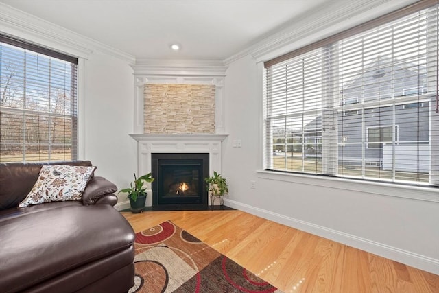 living area with baseboards, a fireplace with flush hearth, wood finished floors, and ornamental molding