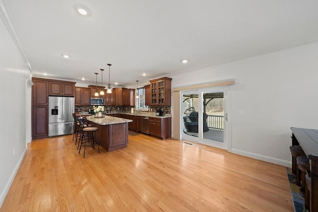 kitchen featuring light wood-type flooring, a breakfast bar, appliances with stainless steel finishes, crown molding, and decorative backsplash