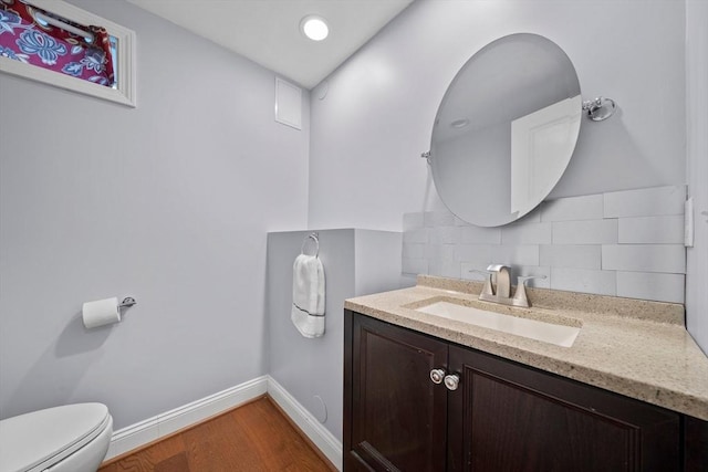 half bath with tasteful backsplash, baseboards, toilet, wood finished floors, and vanity