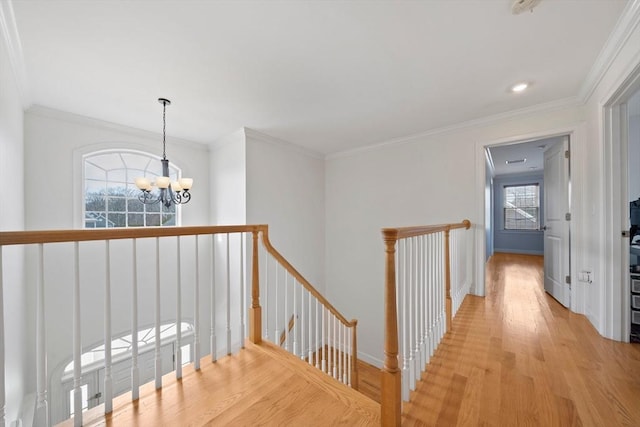 corridor featuring light wood-type flooring, an upstairs landing, a notable chandelier, crown molding, and baseboards