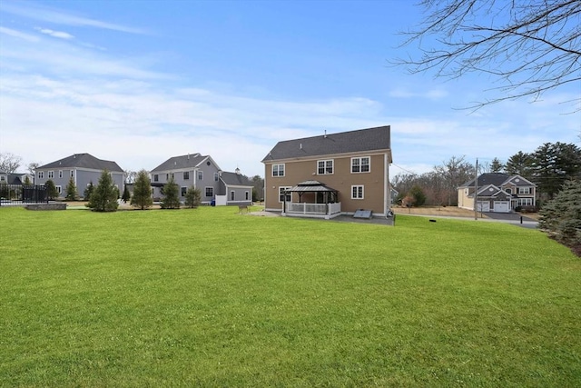 rear view of property featuring a gazebo, a yard, and a residential view