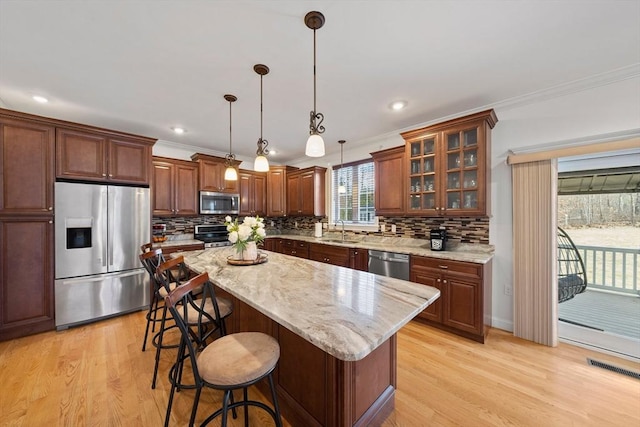 kitchen with a kitchen bar, light wood-type flooring, a sink, stainless steel appliances, and crown molding