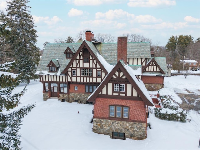 snow covered property with stucco siding, a chimney, and brick siding