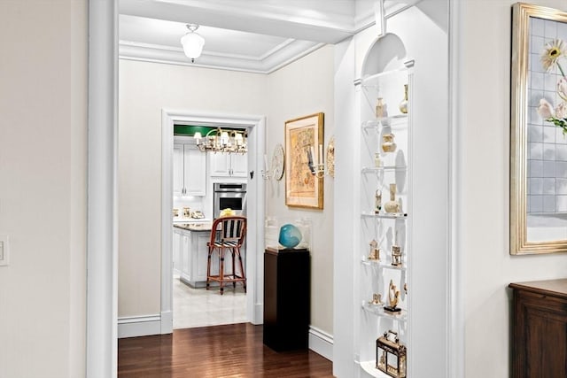 hall featuring crown molding, an inviting chandelier, and dark wood finished floors