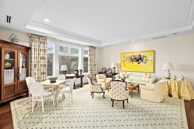 living room featuring ornamental molding, visible vents, a raised ceiling, and wood finished floors
