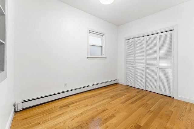 unfurnished bedroom with a closet, baseboards, a baseboard heating unit, and light wood-style floors