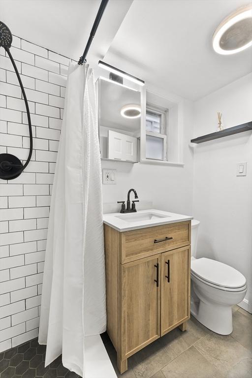 full bath with tiled shower, toilet, and vanity