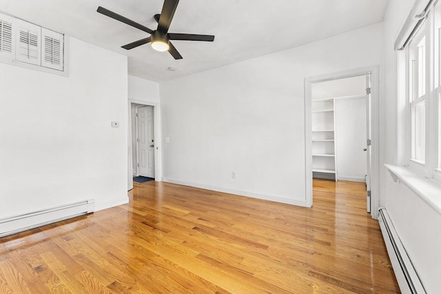 unfurnished bedroom featuring light wood-type flooring, a walk in closet, a baseboard heating unit, baseboards, and baseboard heating