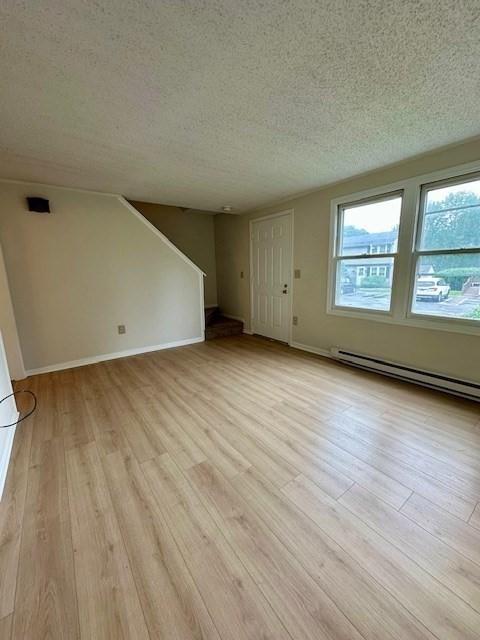 270 Sunderland St Unit 77, Worcester, MA 01604 - unfurnished living room with light wood-type flooring, a textured ceiling, baseboard heating, baseboards, and stairs