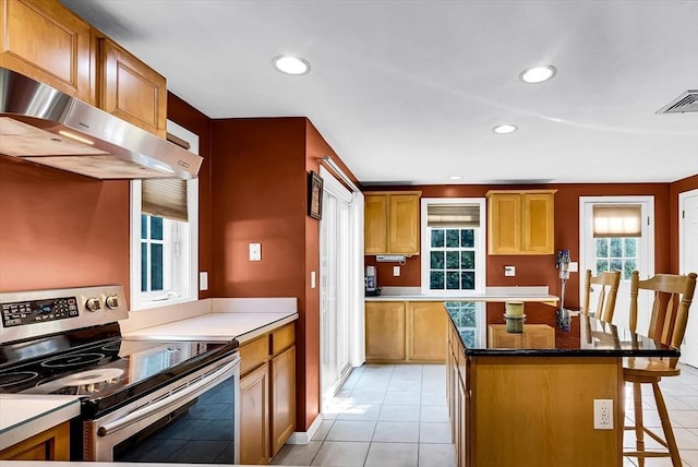 kitchen with stainless steel electric stove, exhaust hood, a kitchen island, a kitchen breakfast bar, and light tile patterned floors