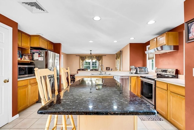 kitchen with appliances with stainless steel finishes, a kitchen island, hanging light fixtures, kitchen peninsula, and a breakfast bar area