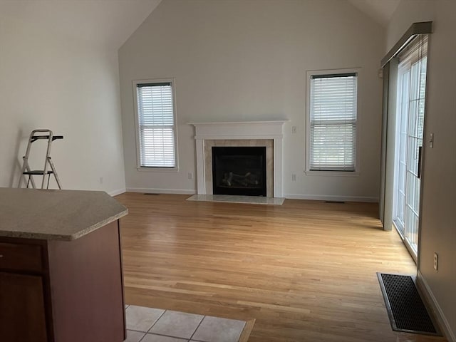 unfurnished living room featuring high vaulted ceiling, a fireplace with flush hearth, visible vents, baseboards, and light wood-type flooring