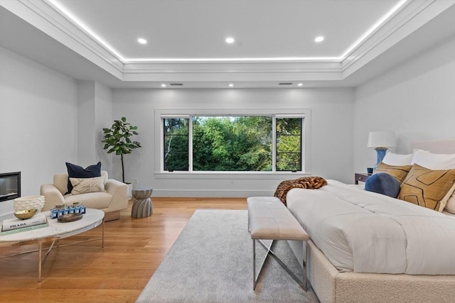 bedroom with light wood-style flooring, multiple windows, a raised ceiling, and crown molding