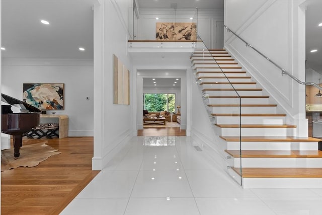 entrance foyer with a towering ceiling, baseboards, ornamental molding, stairway, and light wood-type flooring