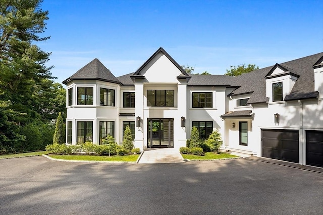 view of front facade featuring a garage, driveway, roof with shingles, and stucco siding