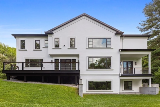 back of property with a balcony, a deck, a lawn, and stucco siding