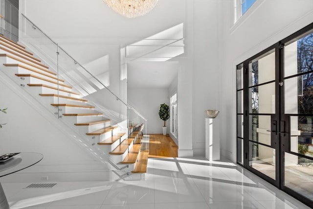 entryway featuring an inviting chandelier, french doors, a high ceiling, and stairs