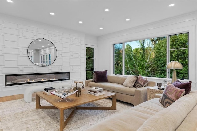 living room with ornamental molding, recessed lighting, a large fireplace, and light wood-style flooring