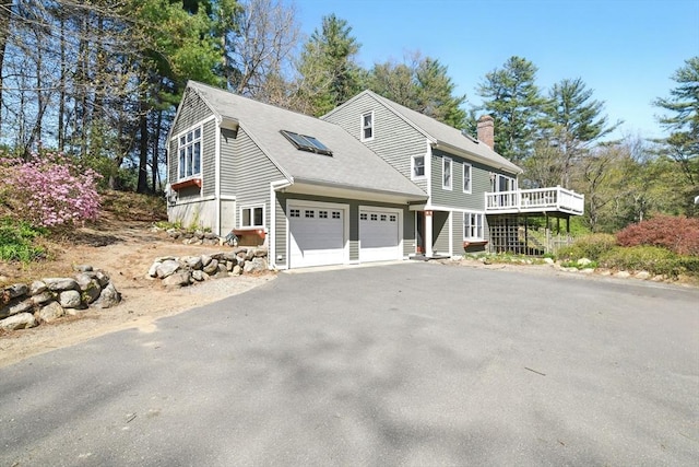 view of front of property featuring a garage, aphalt driveway, a wooden deck, roof with shingles, and a chimney