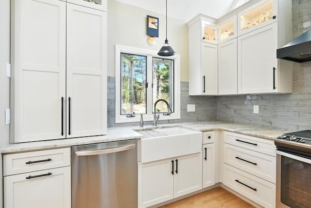 kitchen with light stone countertops, appliances with stainless steel finishes, a sink, wall chimney exhaust hood, and decorative backsplash